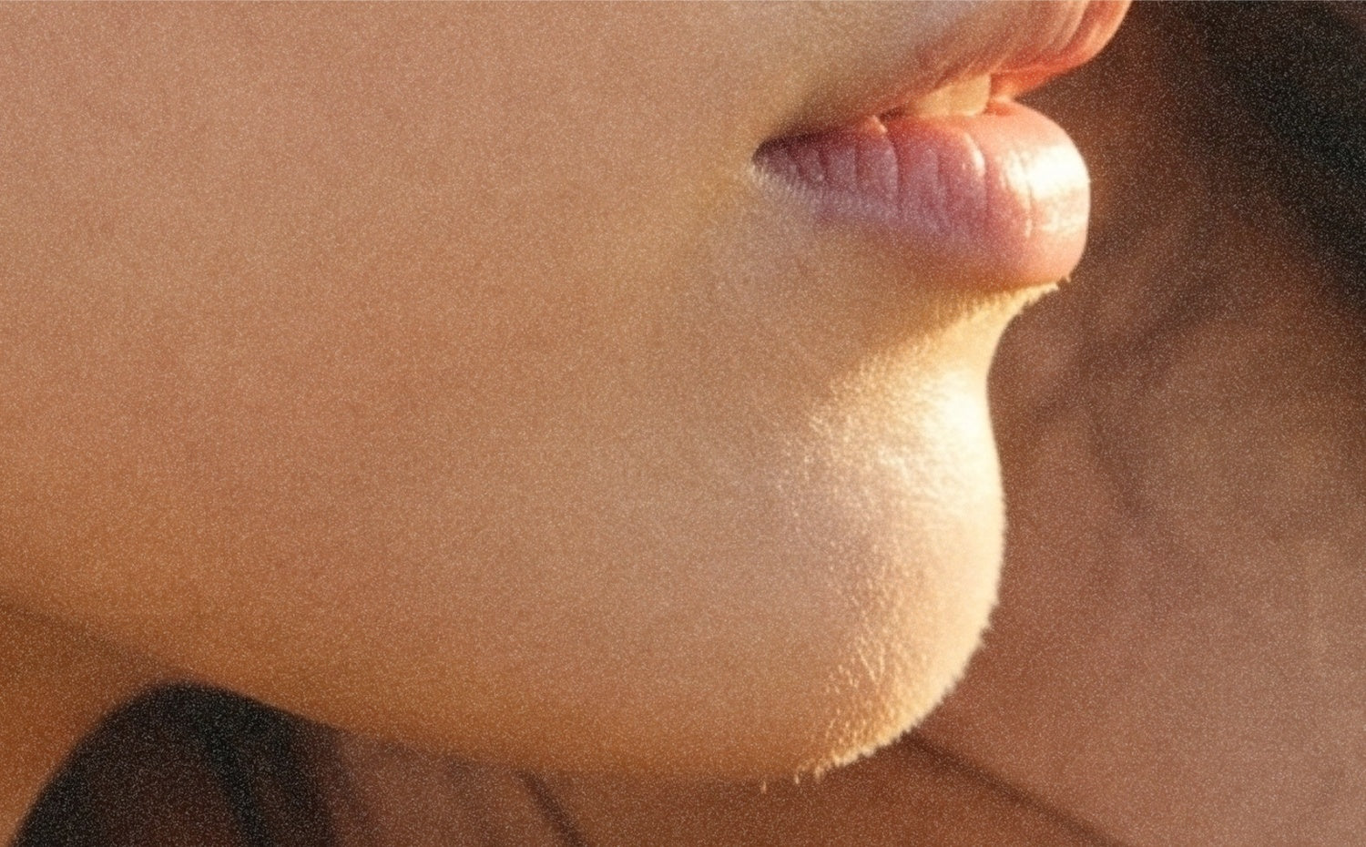 A close, sunlit profile. The lips parted, an orange thread caught in the corner.