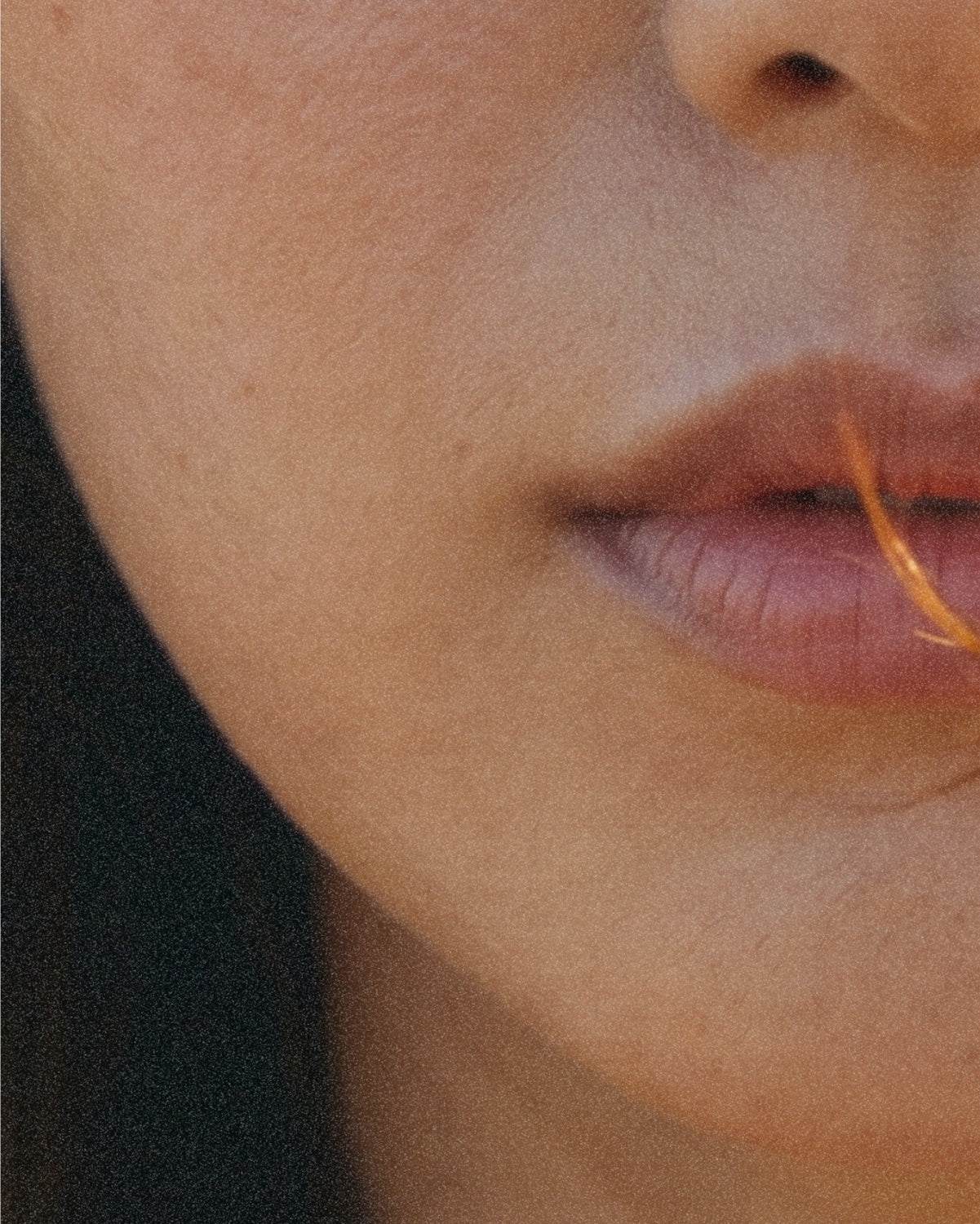 Lips, a soft three-quarter view, an orange thread held between them.